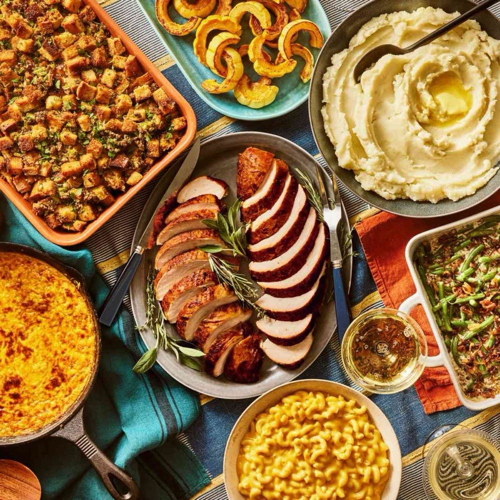 Thanksgiving table spread with sliced turkey, stuffing, mashed potatoes and sides
