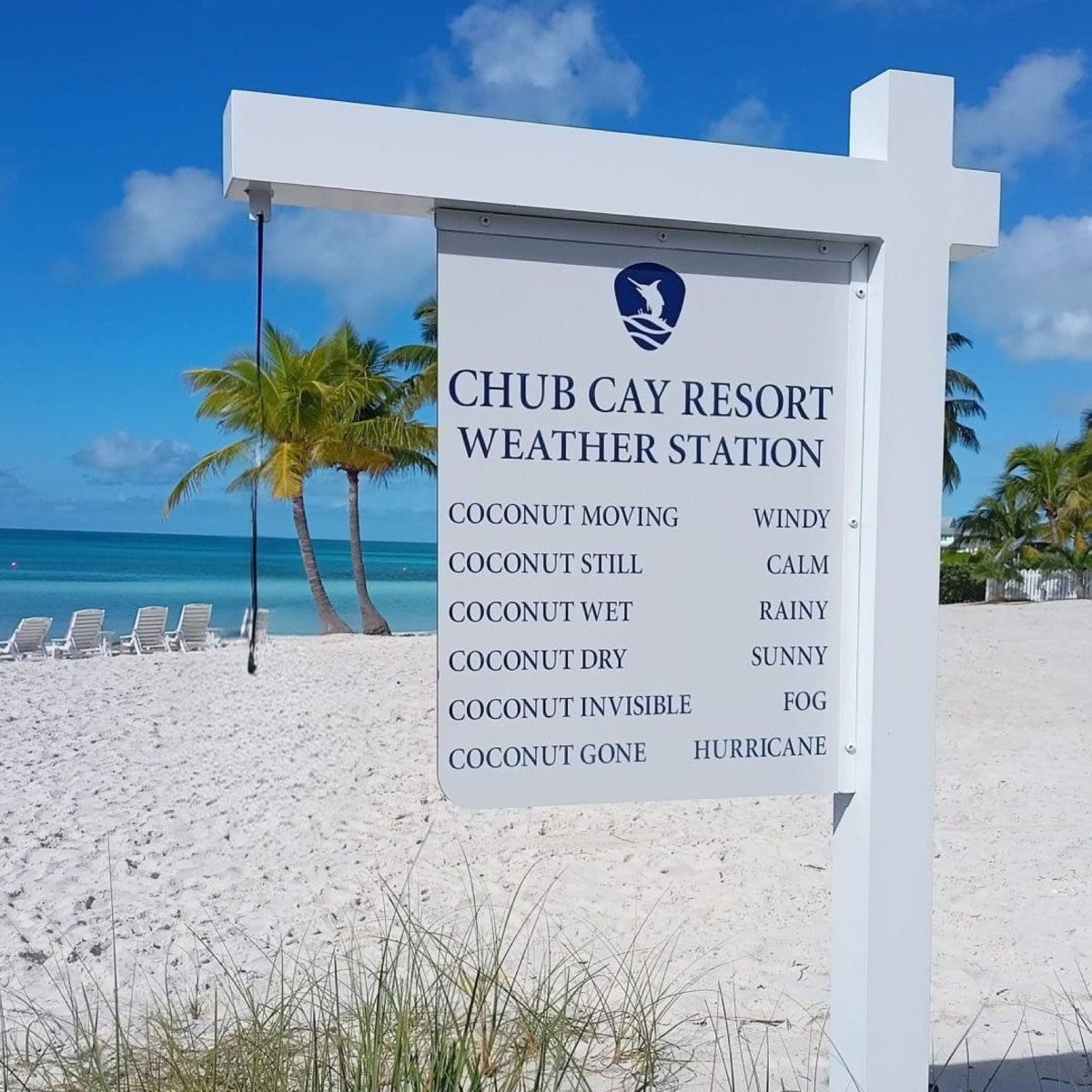 The Chub Cay Resort weather station sign on the beach, with a coconut hanging from a rope