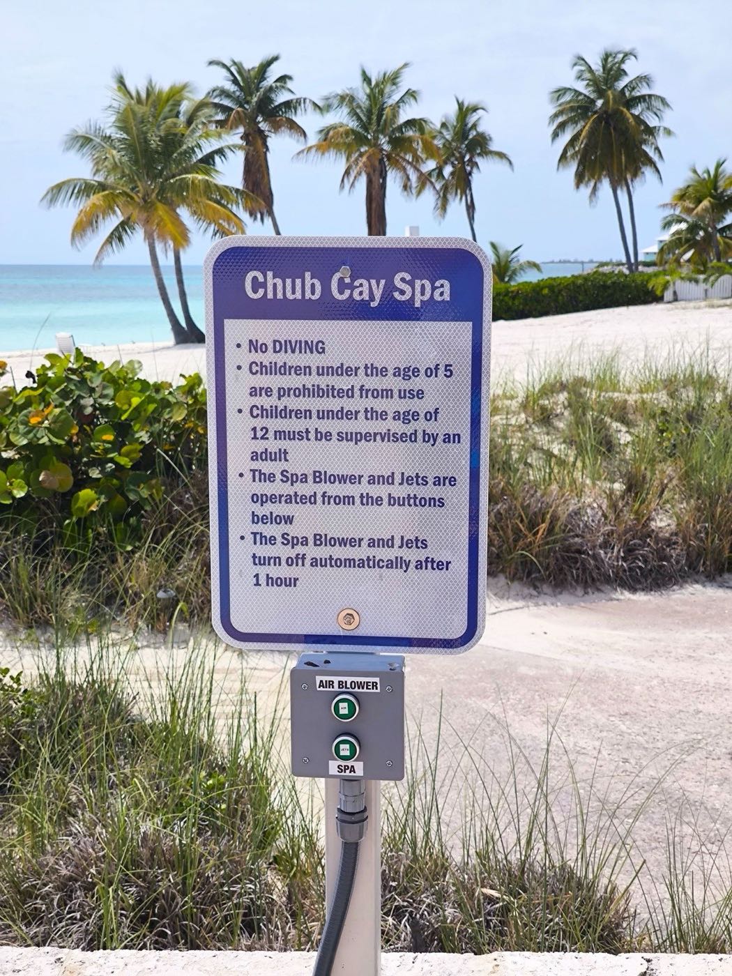 The new Chub Cay Spa sign by the hot tub with air blower and jets buttons, palm trees and beach behind