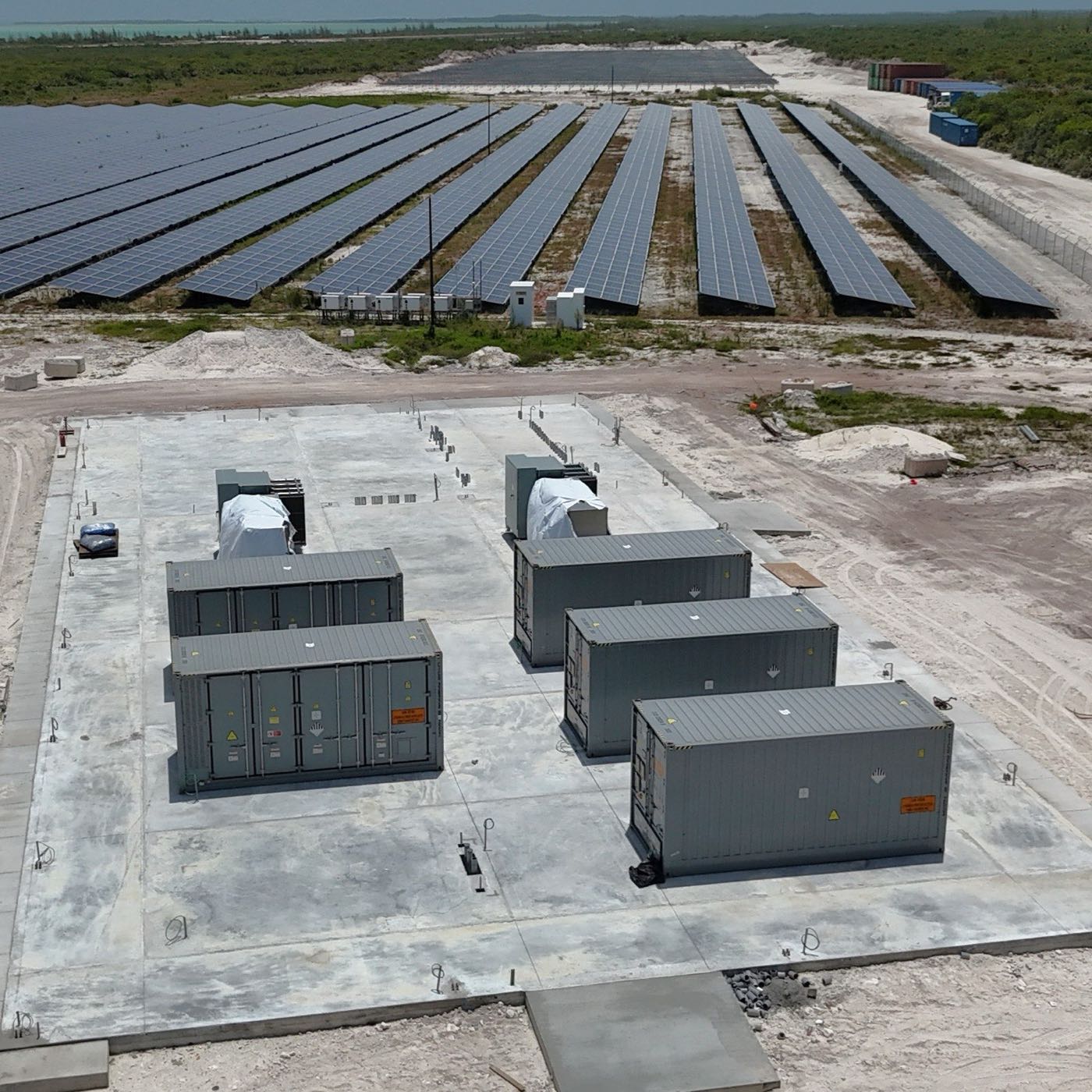 Aerial view of the five container-sized battery units installed at the new solar plant site, with the solar field behind