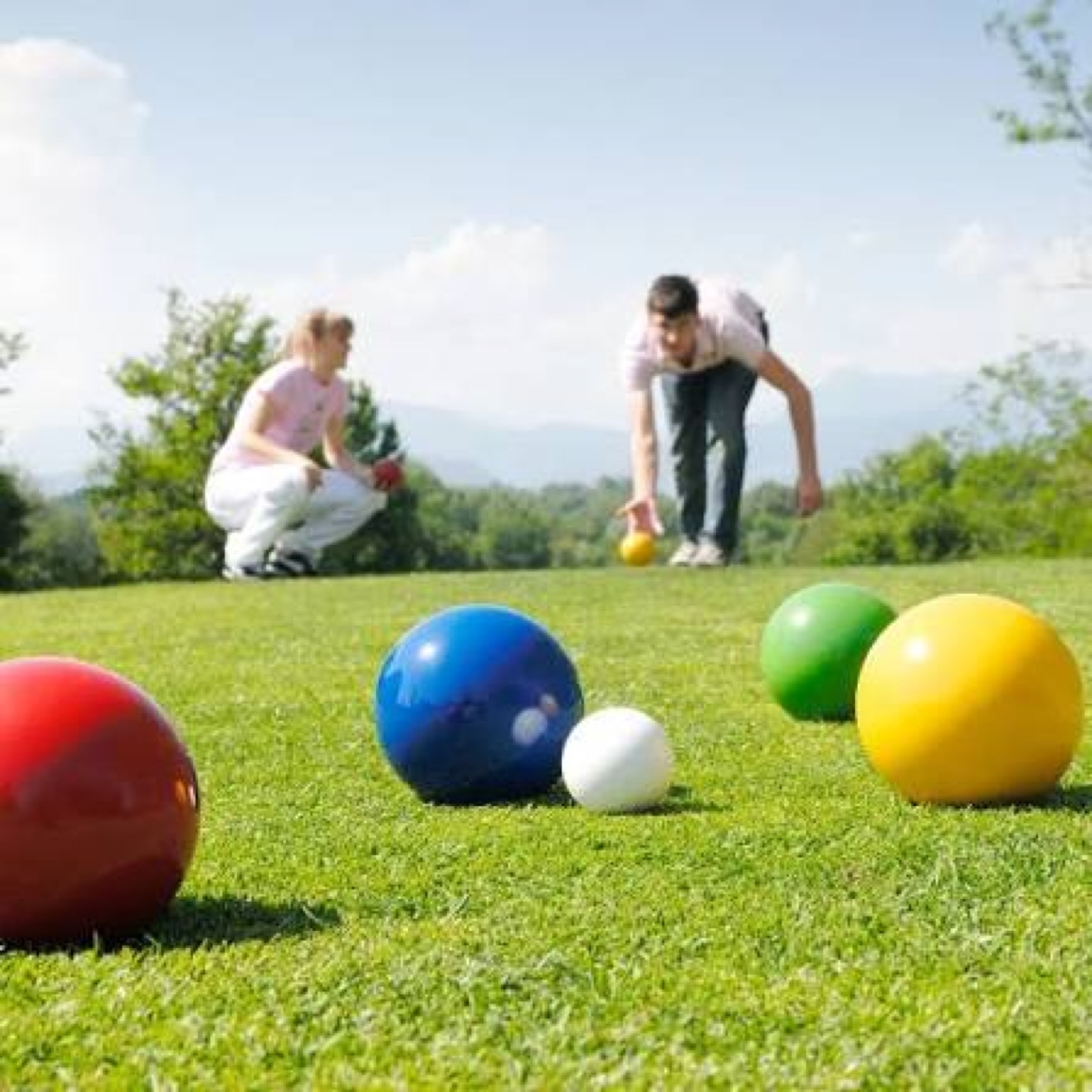Colorful bocce balls on a grass lawn with two players in the background
