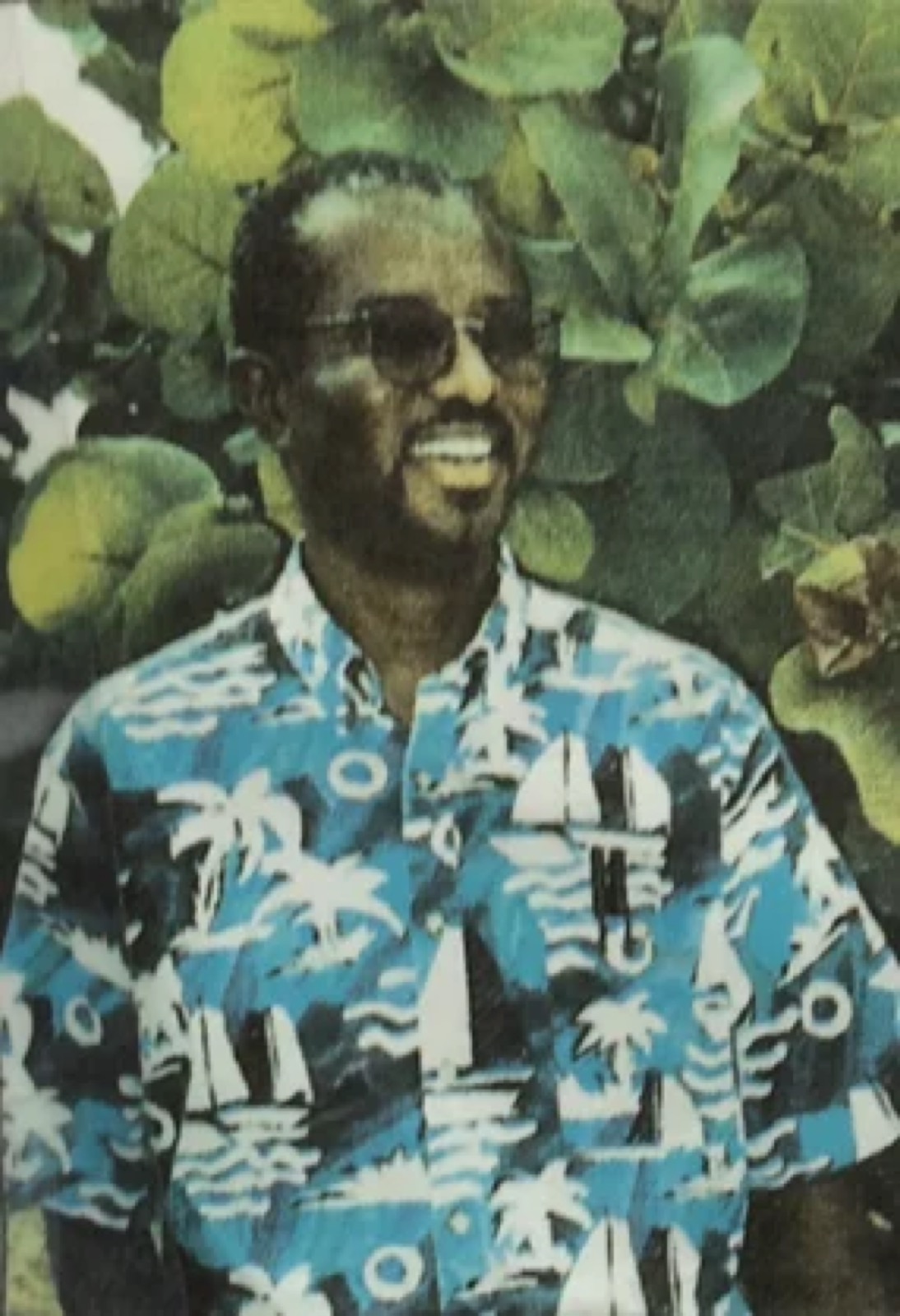 A vintage photograph of a young Remedy in a tropical print shirt among sea grape leaves